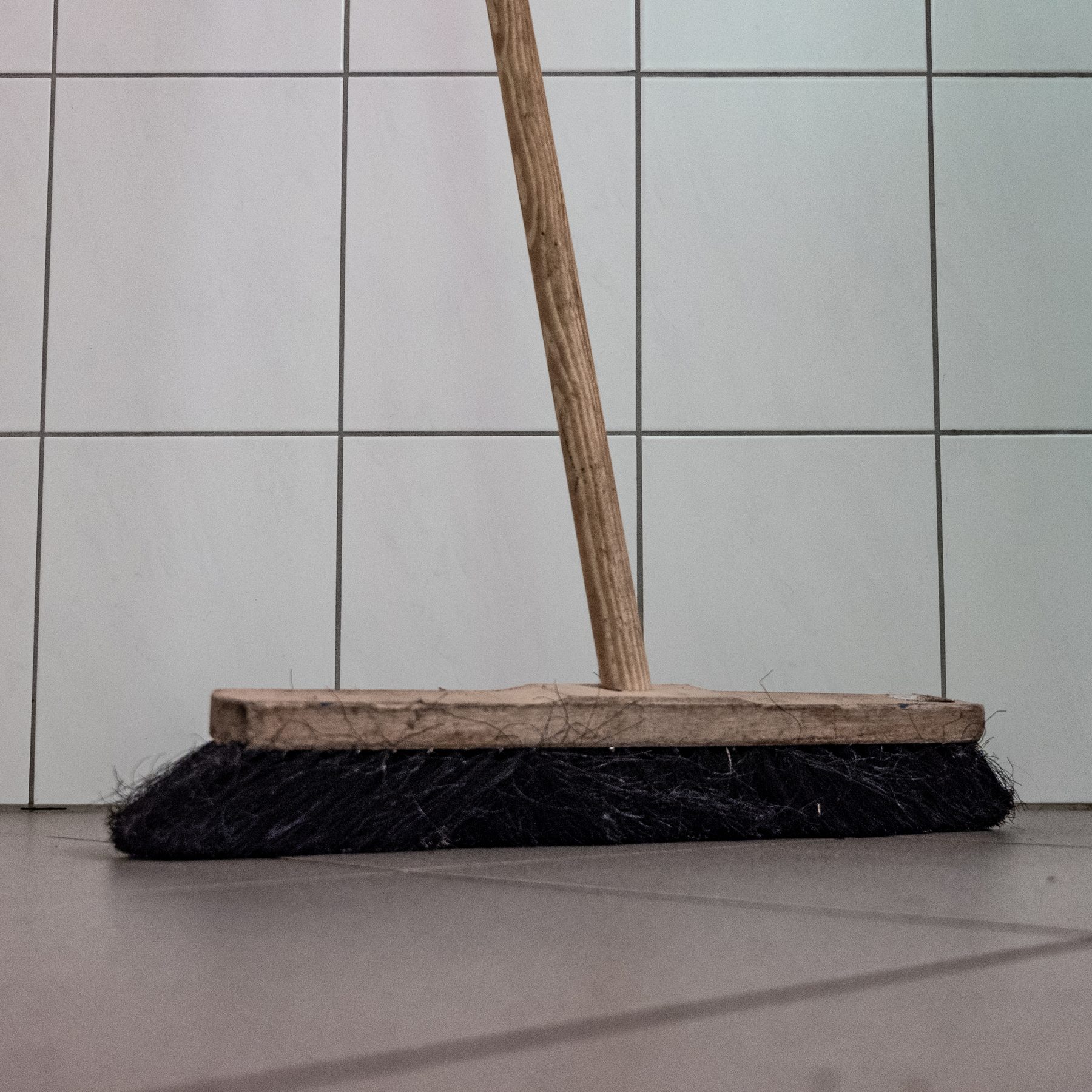 Wooden broom with black organic bristles standing on tiled floor