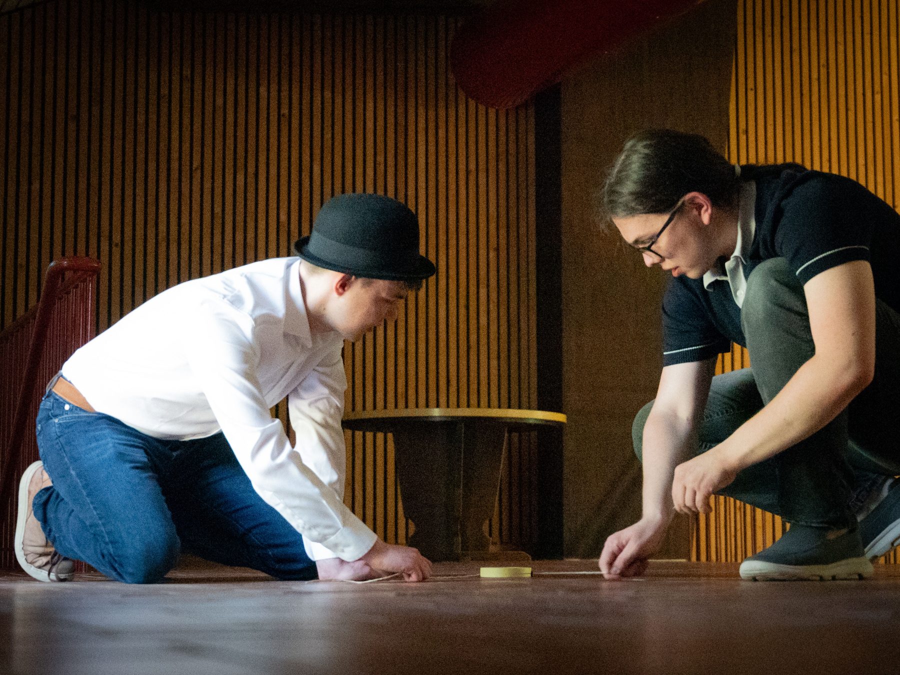 Two people kneeling on the floor right before pulling a Slingshot to shot a flat Quibble towards the photographer