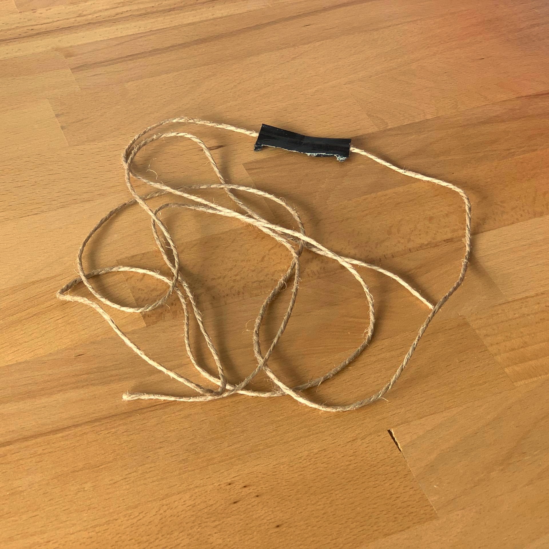 Single string laying cluttered on wooden surface. String has on black stripe of 5x1 cm in the center to hold Quibble.