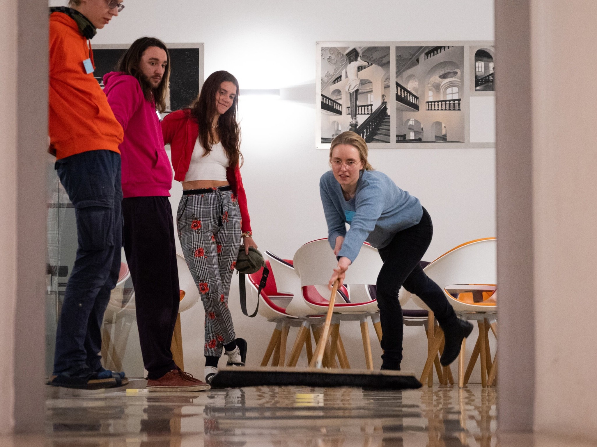 Person pushing Quibble away from herself with broom and much force. Three bystanders observe the shot from the background.